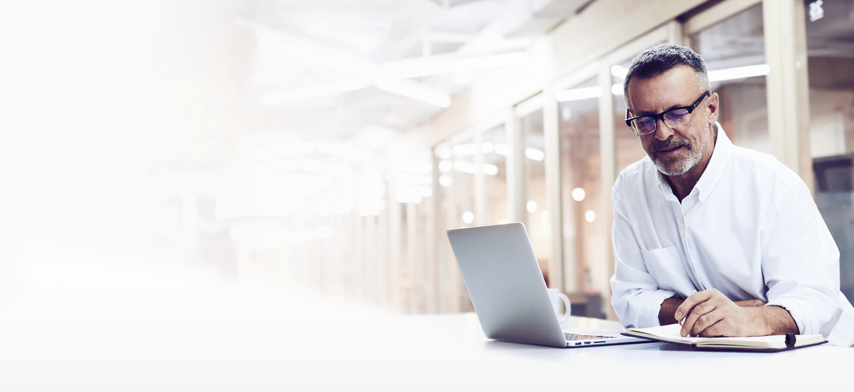 Middle-aged man writing in notebook, working on computer at desk